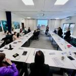 Ludzie siedzący przy stołach w sali konferencyjnej podczas prezentacji.